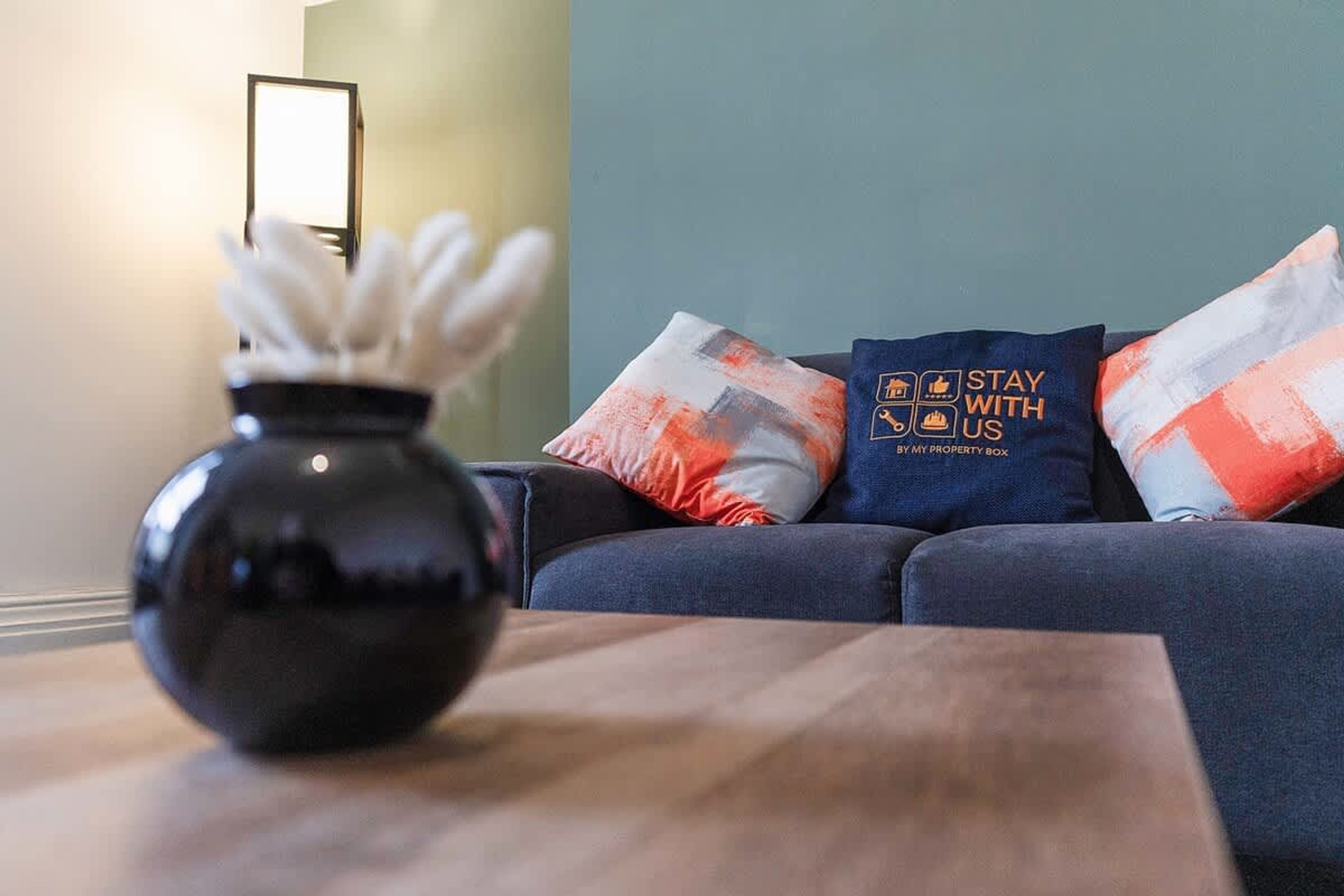 A modern living room with a dark blue sofa, a wooden coffee table, and decorative pillows with a travel-themed design.