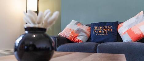 A modern living room with a dark blue sofa, a wooden coffee table, and decorative pillows with a travel-themed design.