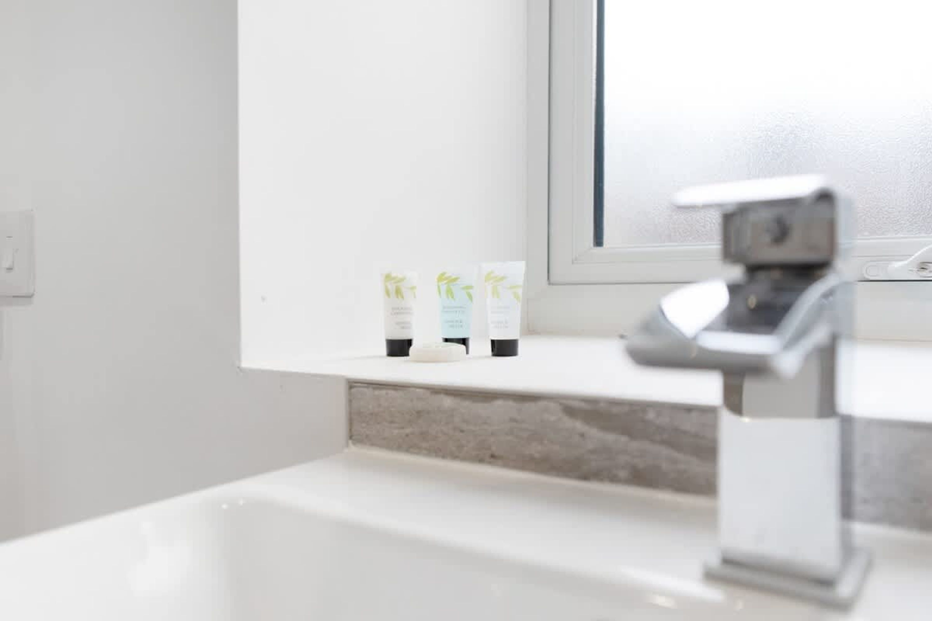 Ett badrum med ett vitt handfat, en spegel och tre flaskor med hygienprodukter på bänkskivan.