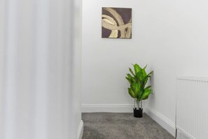 A hallway with a radiator, a potted plant, and a wall-mounted artwork. - Spacious Five Bedroom Family Home Group Stay Wifi (Sunderland)