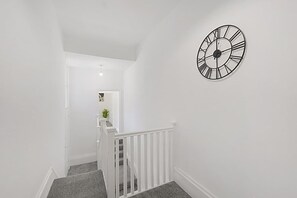 A staircase with a white railing leading to a landing with a clock on the wall. - Spacious Five Bedroom Family Home Group Stay Wifi (Sunderland)