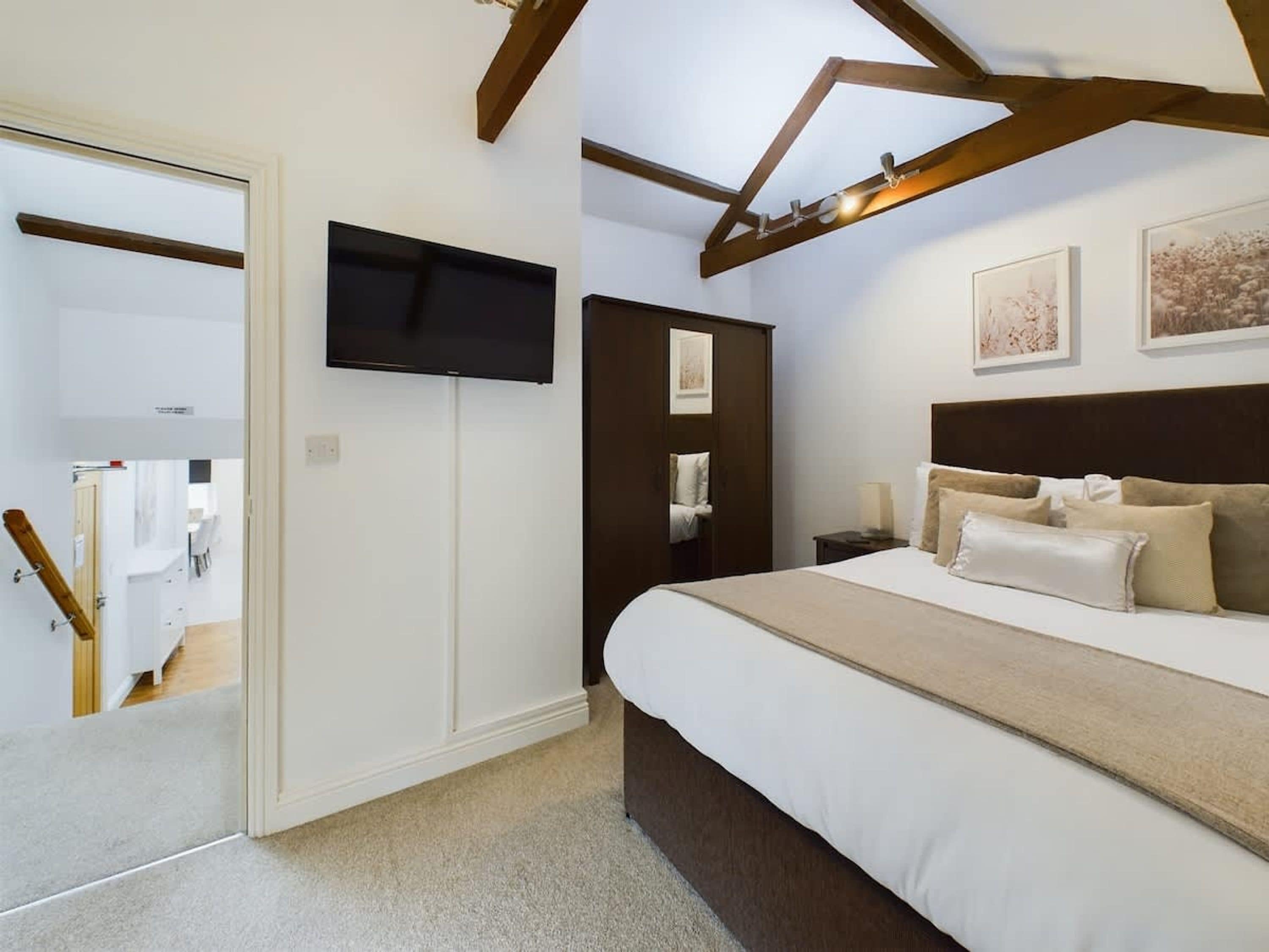 Un dormitorio con cama, televisor, armario y techo con vigas a la vista.