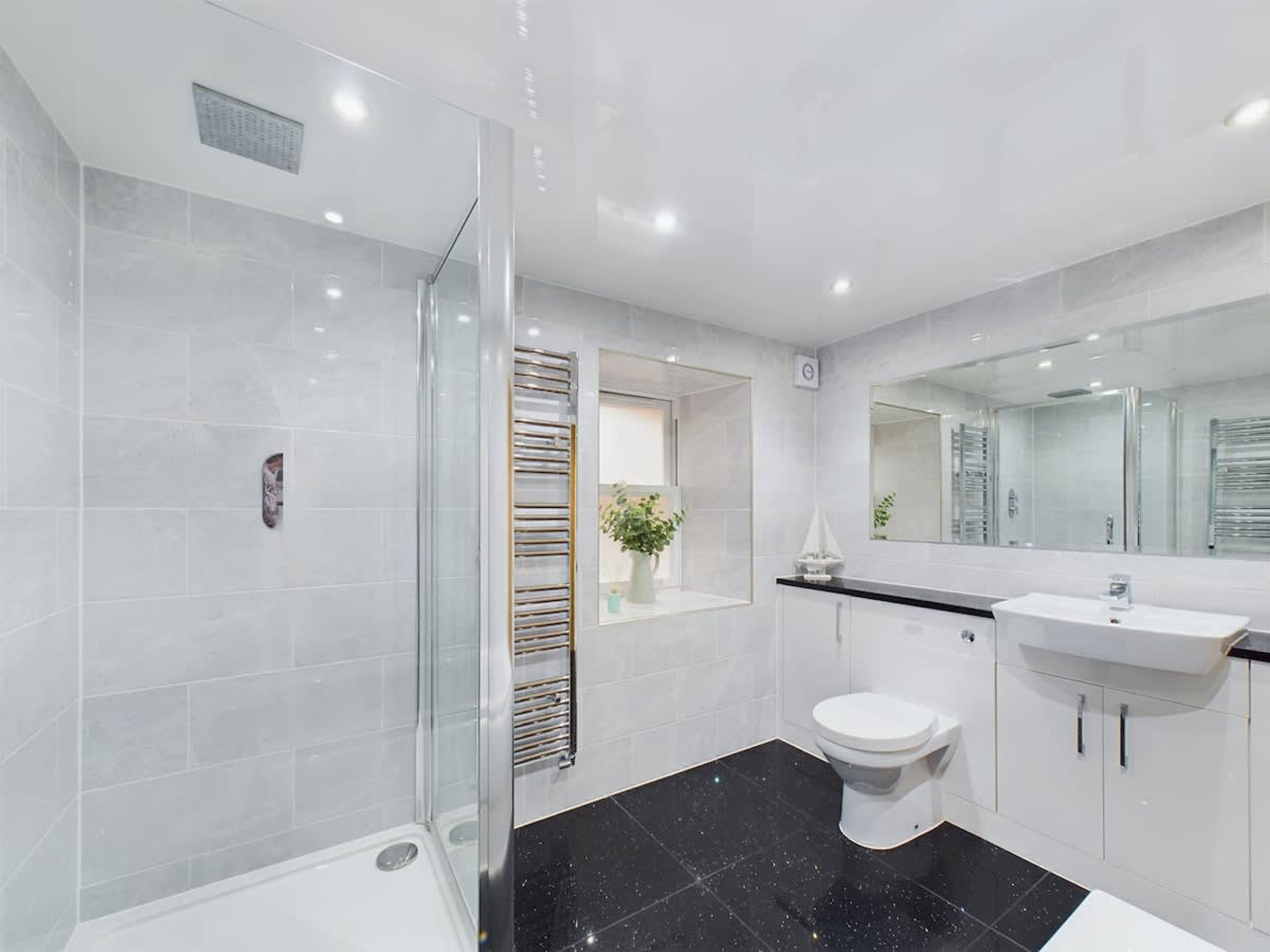 Un baño moderno con cabina de ducha de vidrio, inodoro blanco, lavamanos con espejo y toallero.