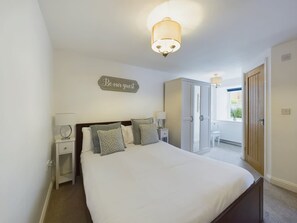 Un dormitorio con cama, mesitas de noche, un armario y un letrero en la pared que dice 'Be our guest'.
