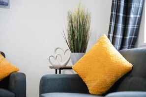 Un salon moderne avec un canapé gris, un objet blanc en forme de cœur posé sur une table et un coussin jaune.
