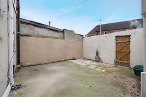 Ein schmaler Außenbereich mit Betonboden, einem Holztor und einer Wand mit rauer Struktur.