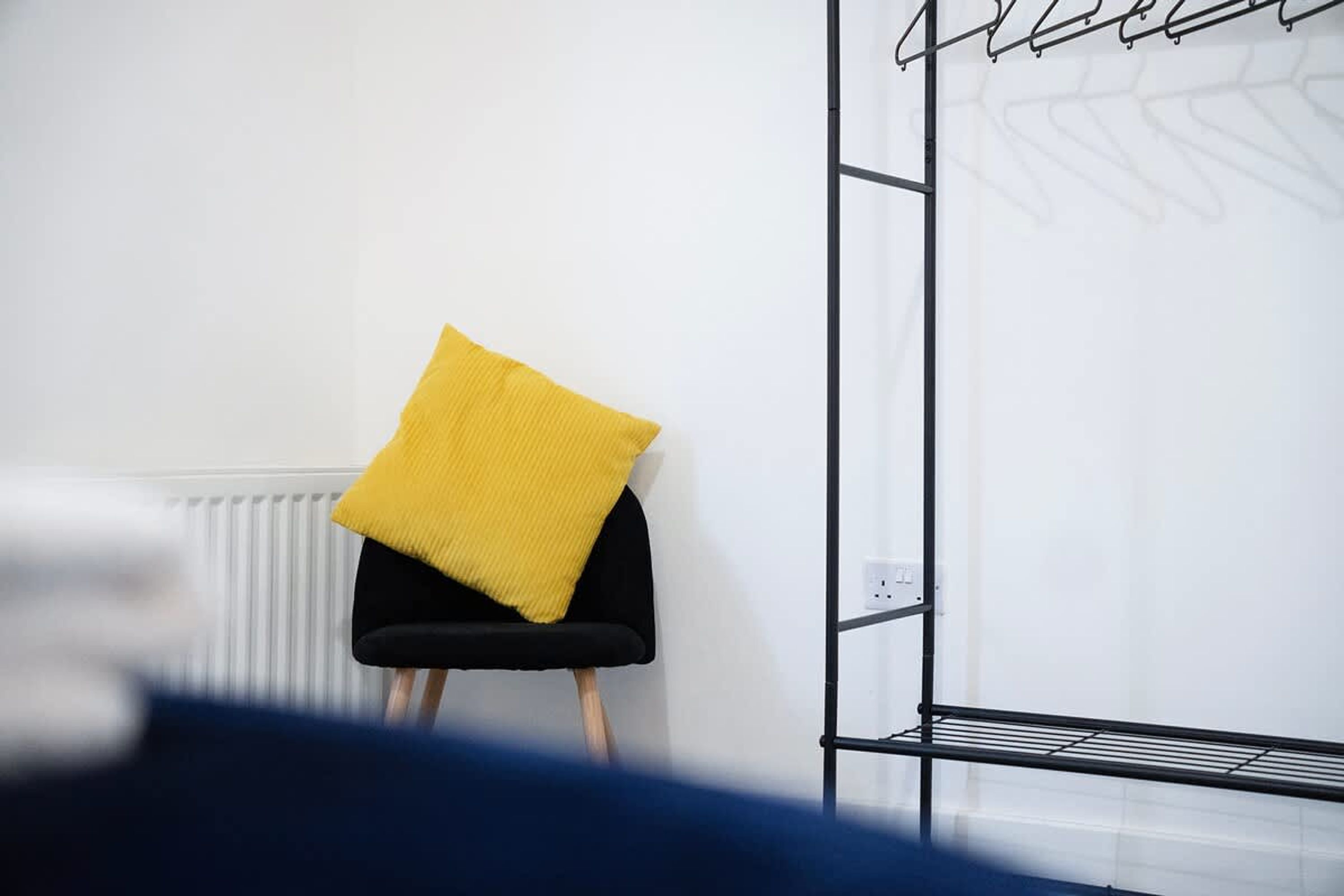 A room with a black chair, a yellow cushion, a white radiator, and a metal rack.