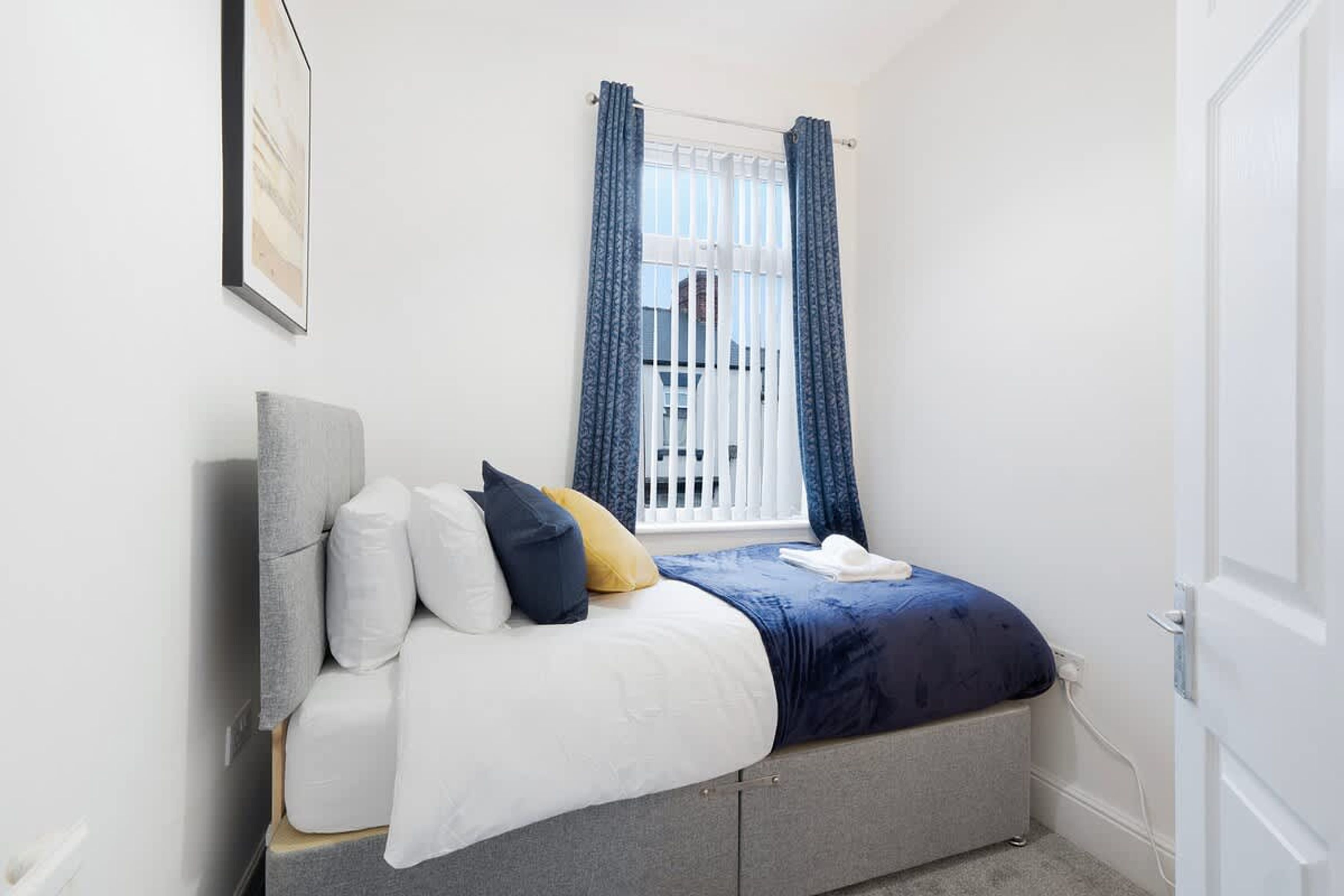 A bedroom with a bed, pillows, a window with curtains, and a door.