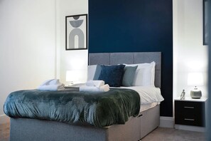 A neatly made bed with pillows and a blanket, a bedside table with a lamp, and a framed picture on the wall. - Stylish Home Near Darlington Town Centre (Darlington)