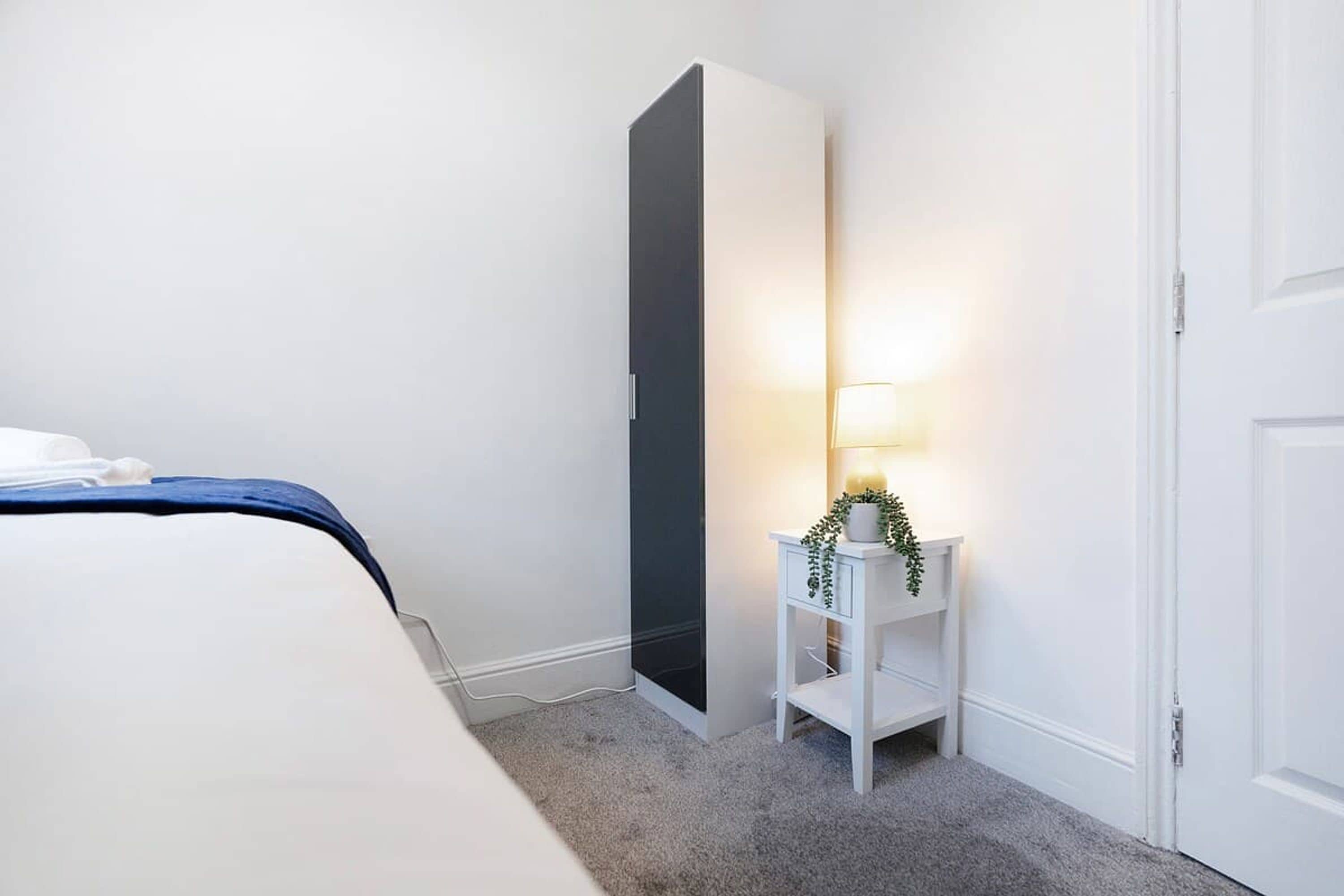 Un dormitorio con cama, armario, mesita de noche con lámpara y una puerta.