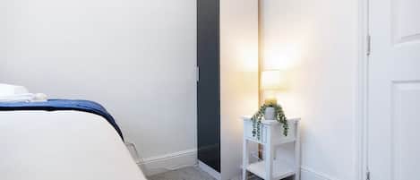 Un dormitorio con cama, armario, mesita de noche con lámpara y una puerta.