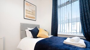 Habitación de hotel con cama, ventana con cortinas, radiador y un cuadro en la pared.