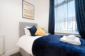 Ein Hotelzimmer mit einem Bett, einem Vorhangfenster, einem Heizkörper und einem gerahmten Bild an der Wand.