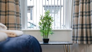 Una habitación con una cama, una mesita con una planta en maceta y una ventana con cortinas.
