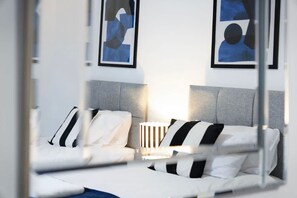 Et hotelværelse med en seng, puder, en sengebordlampe og to abstrakte malerier på væggen.