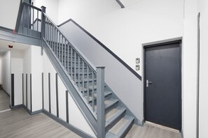 Eine moderne Treppe mit Metallgeländer, einer dunklen Tür und einer hellen Wand.