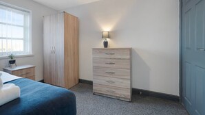Ett sovrum med en säng, en garderob, en byrå, en lampa och ett fönster.