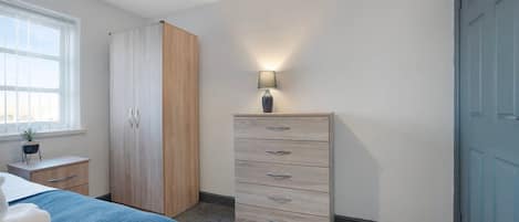 A bedroom with a bed, a wardrobe, a dresser, a lamp, and a window.