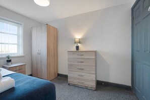 Ein Schlafzimmer mit Bett, Kleiderschrank, Kommode, Lampe und Fenster.