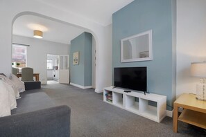 A modern living room with a flat-screen TV on a white stand, a grey sofa, and a wooden side table with a lamp. - 2BR in Brighton Road With Wifi Parking Smart TV (Darlington)