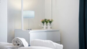 Ein Hotelzimmer mit weißem Schminktisch, einem Spiegel, einer Lampe und einer Vase mit Blumen.