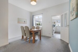 A dining area with a table and chairs, a window with a view, and a kitchen visible through an open door. - 2BR in Brighton Road With Wifi Parking Smart TV (Darlington)