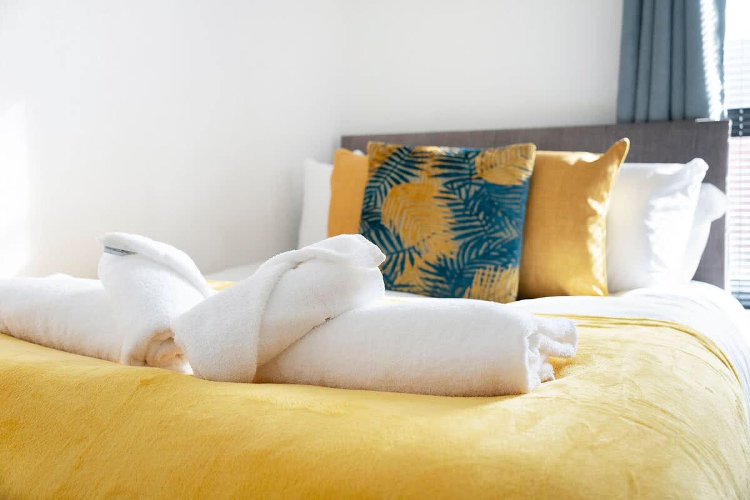Un lit bien fait, avec des serviettes blanches, une couvre-lit jaune et des coussins à motifs.