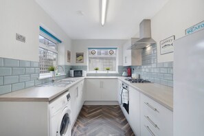 A compact kitchen with a washing machine, a microwave, and a stove. - 2BR in Brighton Road With Wifi Parking Smart TV (Darlington)