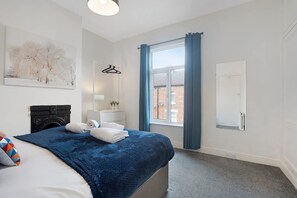 A hotel room with a bed, a window with curtains, a painting on the wall, and a door. - 2BR in Brighton Road With Wifi Parking Smart TV (Darlington)