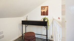 Ein Zimmer mit einem schwarzen Schreibtisch, einem gewebten Hocker, einer Wandpflanze und einem Gemälde von einem Pferd.