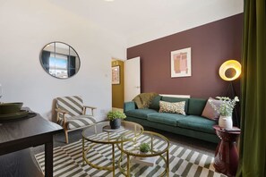 Ein modernes Wohnzimmer mit einem grünen Sofa, einem gestreiften Sessel, einem runden Spiegel, einem runden Couchtisch und einer Stehlampe.