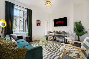 A living room with a sofa, coffee table, TV, and a dining area with a table and chairs. - Modern 4BR With Easy Access to Town and Station (Darlington)