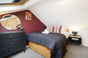 Ein Schlafzimmer mit Bett, Kommode, Nachttisch, Lampe, Spiegel und einem Bild an der Wand.