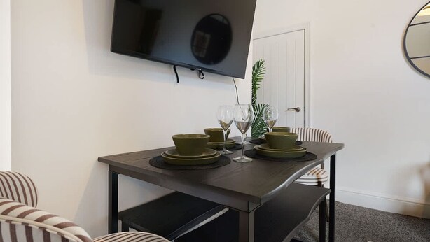 Ein Essbereich mit einem Tisch für zwei Personen, einem an der Wand befestigten Fernseher und einer Tür im Hintergrund.