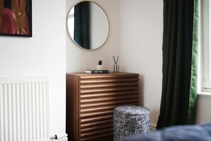 Une chambre avec une commode en bois, un miroir rond, une petite plante et un livre intitulé « NEW YORK » posé sur la commode.