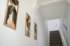 Eine Treppe mit Handlauf und einer Wand, an der drei gerahmte Kunstwerke hängen.