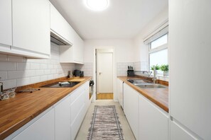 Eine schmale Küche mit weißen Schränken, einer Holz Arbeitsplatte und einem kleinen Fenster.