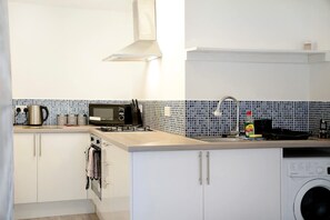 Uma cozinha compacta com armários brancos, micro-ondas, chaleira e máquina de lavar.