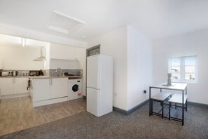 A modern kitchen with white cabinetry, a built-in washing machine, and a small dining area with a table and bench. - 2 Bedroom With Private Parking and Free Wifi (Stockton-on-Tees)