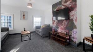Una sala de estar moderna con un sofá gris, una pequeña mesa de madera y un gran mural floral en la pared.