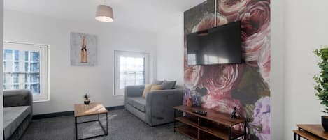 A modern living room with a grey sofa, a small wooden table, and a large floral mural on the wall.