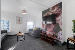 Ein modernes Wohnzimmer mit einem grauen Sofa, einem kleinen Holztisch und einer großen Wandmalerei mit floralem Muster.