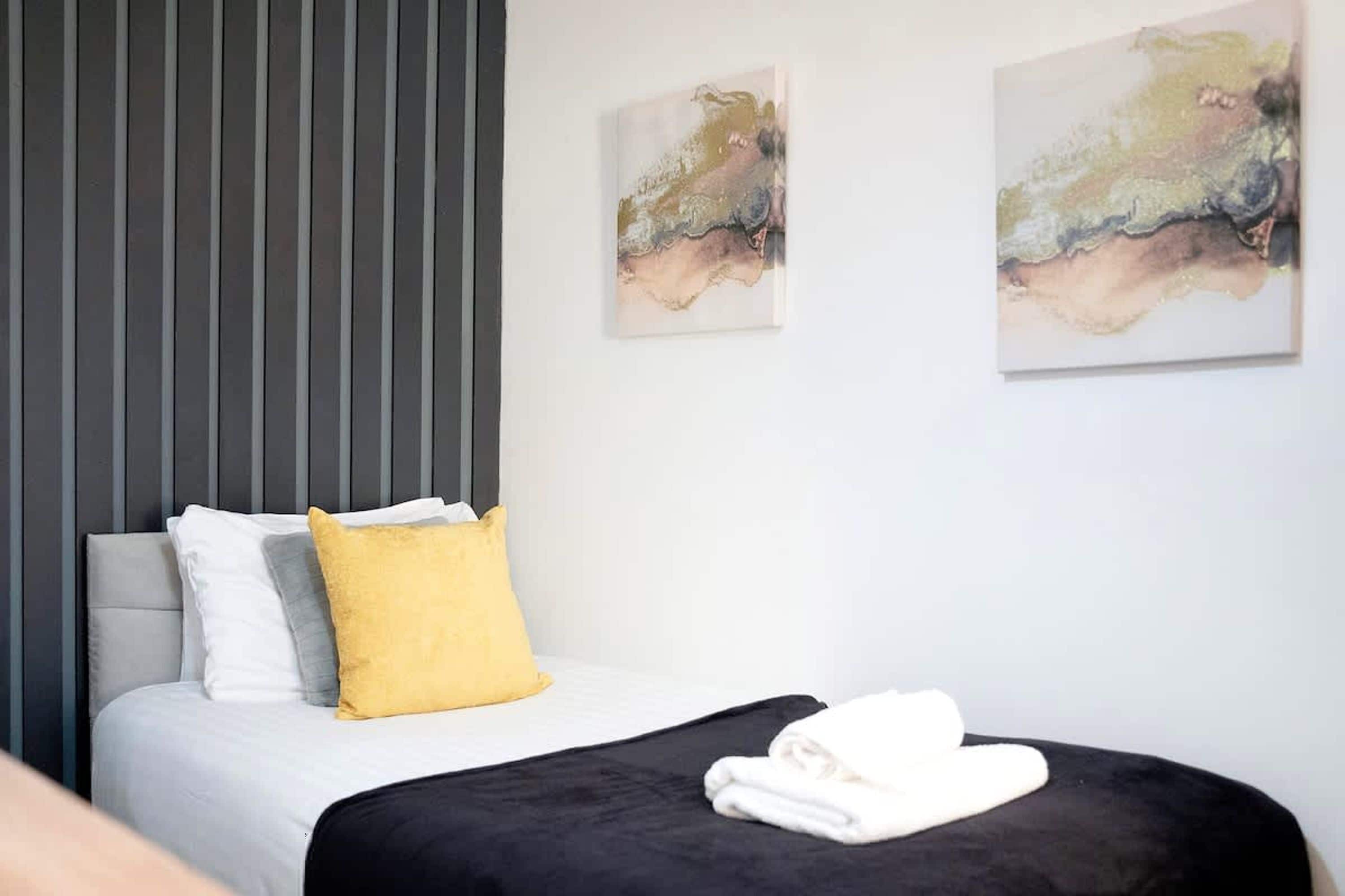 Ein Hotelzimmer mit einem Bett, einem grauen Kopfteil, einer weißen Wand und zwei abstrakten Bildern.