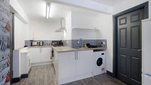 Una cocina compacta con armarios blancos, microondas, hervidor y lavadora.