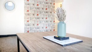 Una habitación con una mesa de madera, un florero con plantas secas y un papel tapiz estampado.