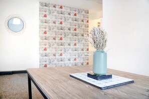 Ein Zimmer mit einem Holztisch, einer Vase mit Trockenpflanzen und einer Wand mit Muster.