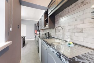 A modern kitchen with a marble countertop, stainless steel sink, and grey tiled backsplash.
