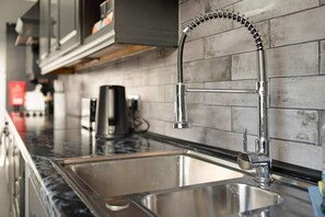 Eine moderne Küche mit Spüle aus Edelstahl, einem Wasserhahn mit flexiblem Schlauch und einer Kaffeemaschine auf der Arbeitsfläche.