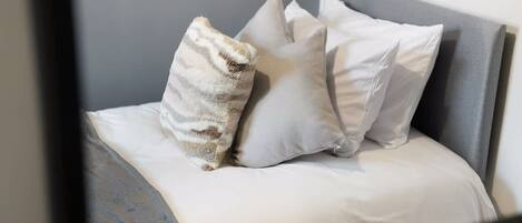 A bed with a grey headboard and white bedding, accompanied by two pillows.