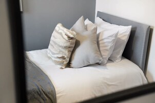 A bed with a grey headboard and white bedding, accompanied by two pillows.